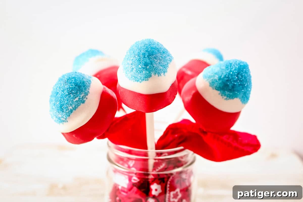 Red, white, and blue covered strawberries on sticks in a mason jar. The mason jar has a red bandana stuffed in it.