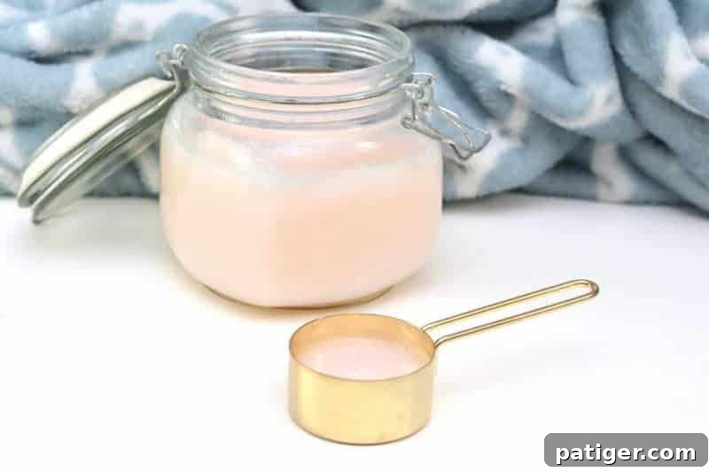 A bottle of homemade fabric softener next to a small bowl with the ingredients: hair conditioner, white vinegar, and baking soda. The setting suggests a clean, DIY approach to laundry care.