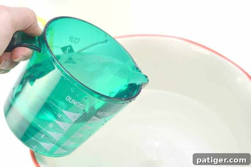 Adding distilled white vinegar to a bowl of hot water as part of the DIY fabric softener preparation.