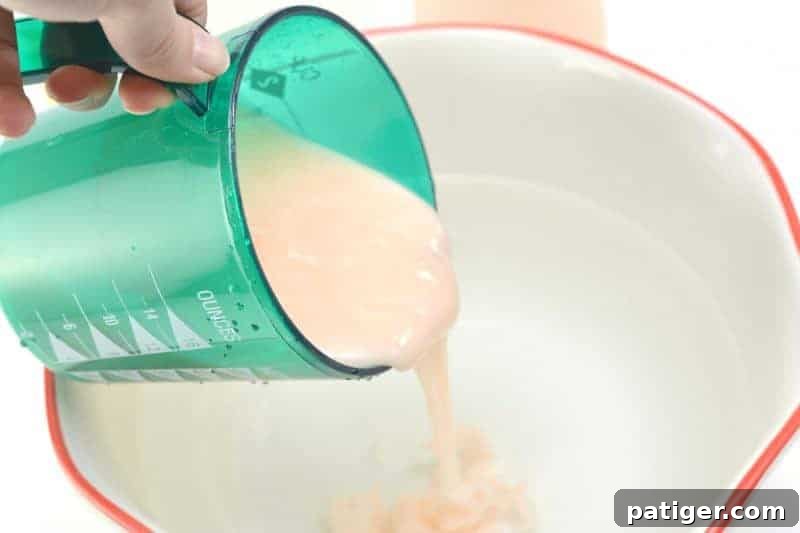 Stirring hair conditioner into the mixture of hot water and vinegar in a large bowl to create homemade fabric softener.