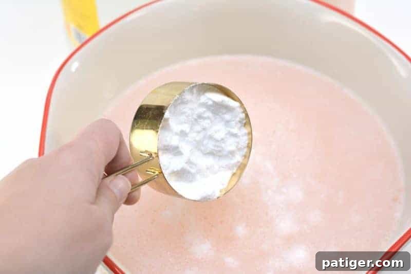 Slowly adding baking soda to the fabric softener mixture, observing the gentle fizzing reaction in the bowl.
