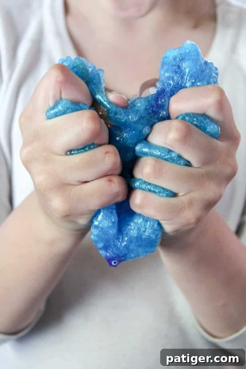 Kids hands playing with bright blue ocean slime, pulling out tiny toy fish and exploring its texture.