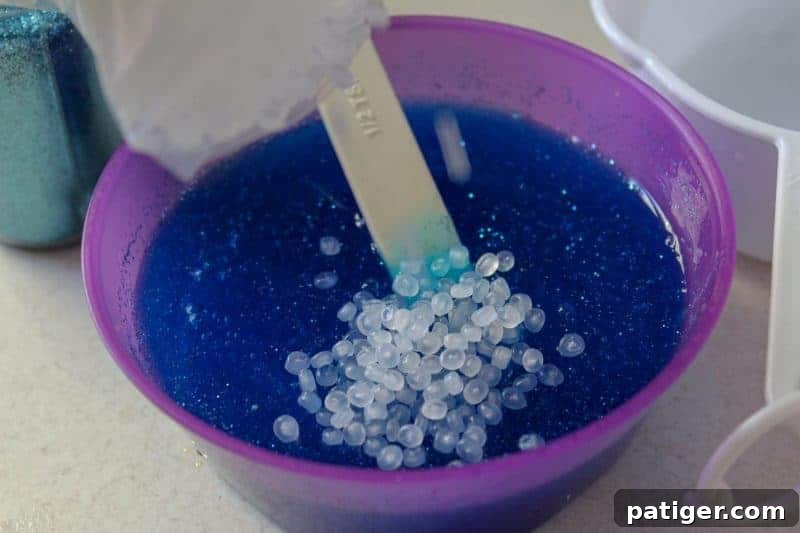 Gently incorporating clear fishbowl beads into the forming ocean slime to add texture.