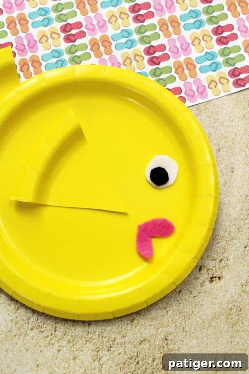 Playful Paper Plate Fish Creations 7 Completed paper plate fish with a child's hand gluing the last colorful paper wedge fin onto its body, showcasing the final assembly step.