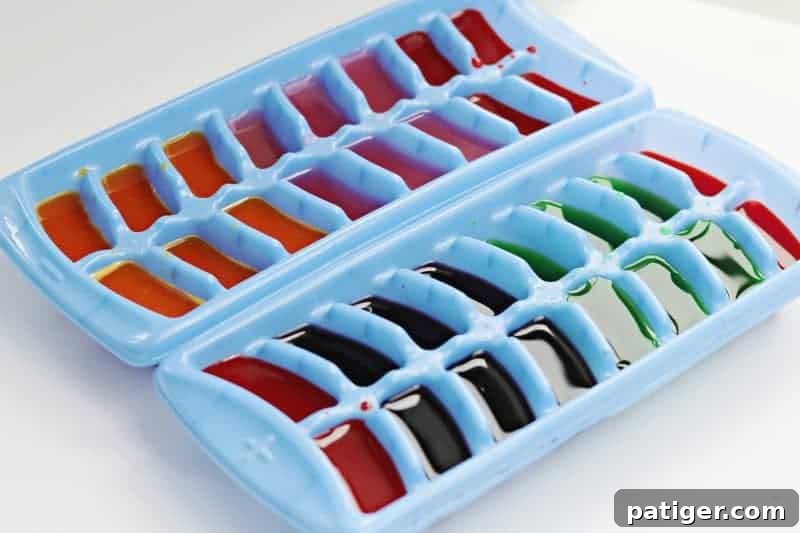 Preparing colored ice cubes for baby sensory play: a hand fills an ice cube tray with vibrant liquid made from drink mix and water.