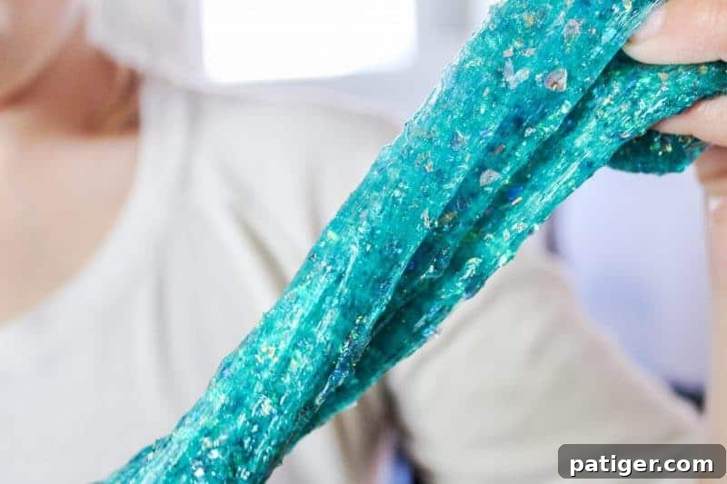 Child's hands stretching shimmery borax-free mermaid slime, showcasing its elasticity.