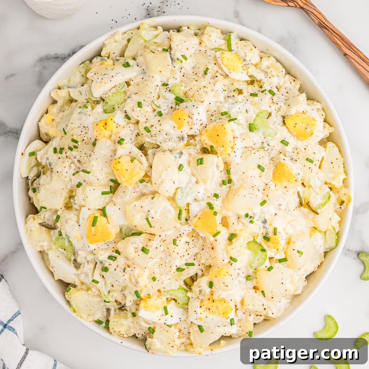 Overhead view of old fashioned potato salad with egg in a white bowl, garnished with a sprinkle of paprika.