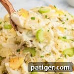Wooden spoon lifting a spoonful of creamy old fashioned potato salad.