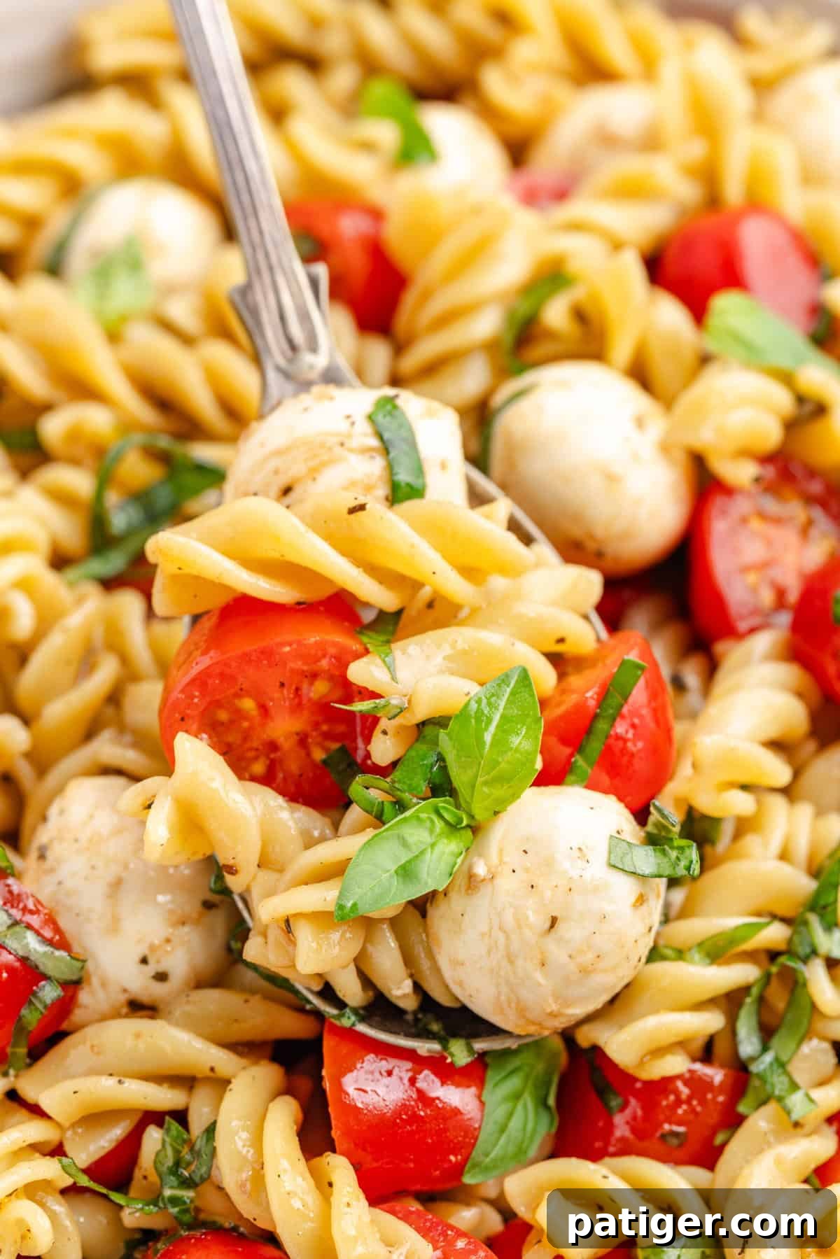 Sun-Kissed Caprese Pasta Salad 7 Close-up of a fork lifting a bite of caprese pasta salad with tomato, mozzarella, and basil.