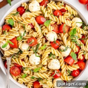 Caprese Pasta Salad with rotini pasta, mozzarella balls, fresh basil, and tomatoes in a large bowl