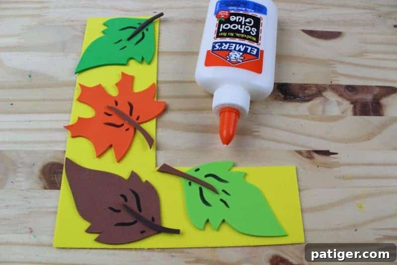 Gluing the decorated craft foam leaves onto the large cut-out letter L, completing the Letter L is for Leaf craft.