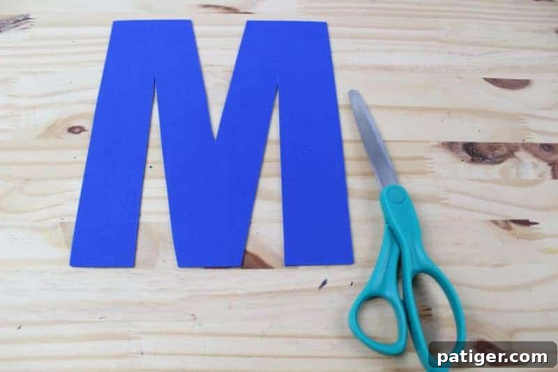 The traced letter M being cut out from craft foam, developing fine motor skills for preschoolers.