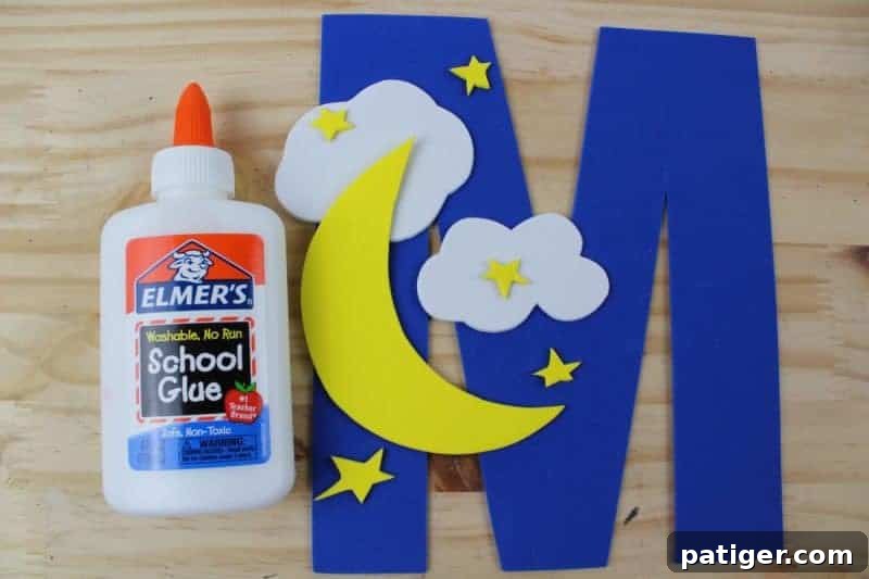 Clouds, a moon, and stars being glued onto a large craft foam letter M, showing a child's progress in their Letter M is for Moon craft.