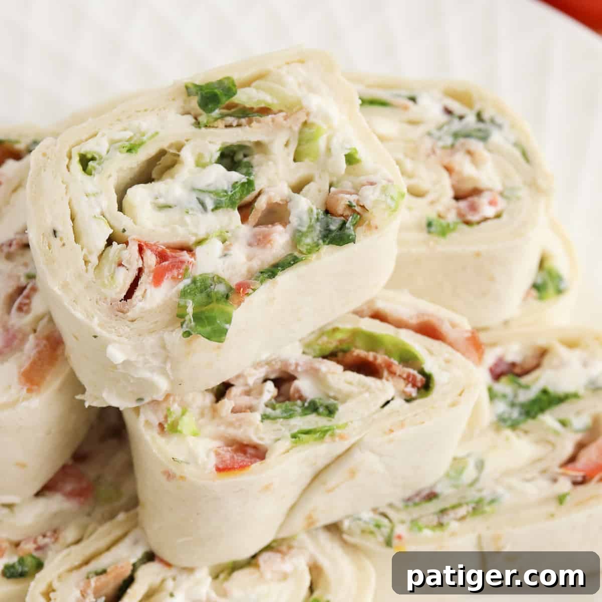 Ranch BLT Pinwheels made with flour tortillas, bacon, lettuce, tomatoes, and ranch dressing stacked on a white plate.
