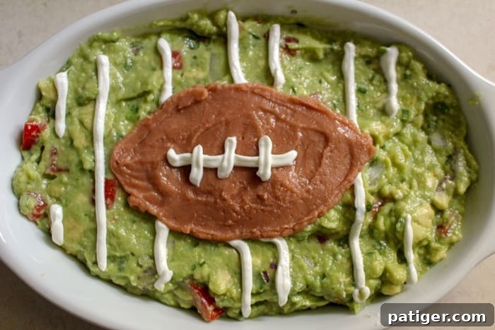 The fully decorated guacamole football field appetizer, featuring sour cream yard lines and refried bean football with white sour cream stitching, ready to serve.