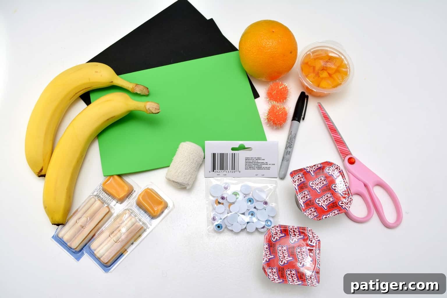 A flat lay showing craft supplies needed for Halloween snacks: gauze, googly eyes, craft foam, hot glue gun, and marker