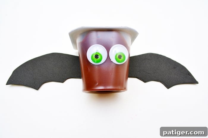 A chocolate pudding cup decorated as a bat with googly eyes and black craft foam wings