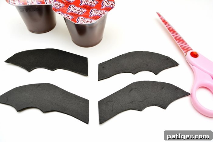 Step-by-step image showing how to cut bat wings from black craft foam for a pudding cup Halloween snack