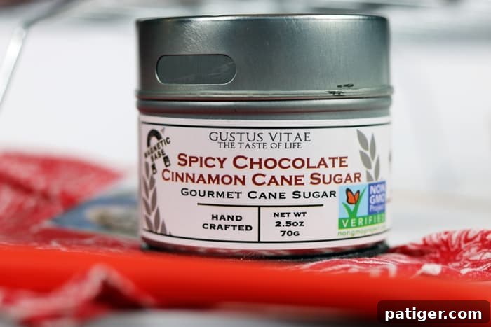 A close-up of the Gustus Vitae spicy chocolate cinnamon cane sugar jar, highlighting its unique blend of flavors. The rich, dark sugar crystals flecked with cinnamon and a hint of spice promise to elevate any dish, making it a star ingredient for adventurous home bakers looking to add depth and warmth to their recipes.
