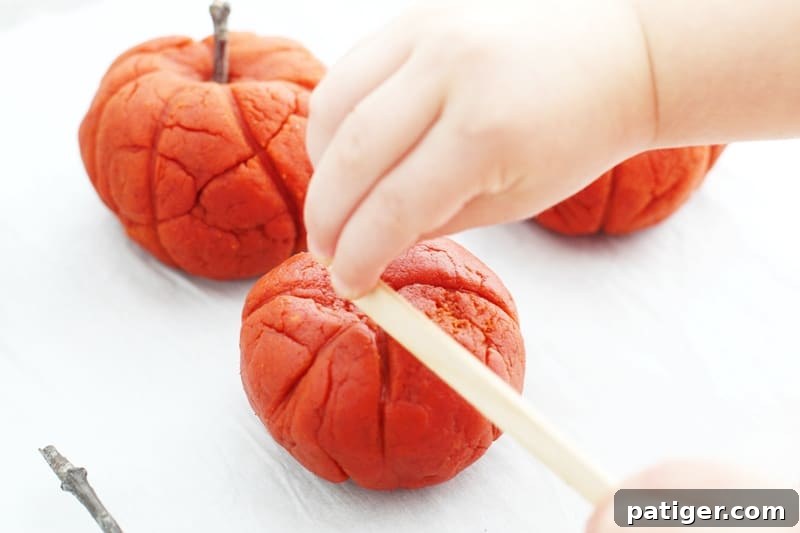 Sensory Pumpkin Spice Playdough 9 Child using natural elements like leaves and twigs to decorate pumpkin playdough