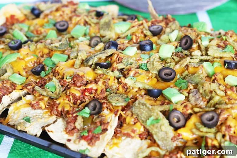 Loaded nachos on a sheet pan topped with a vibrant array of melted cheese, savory beef, sliced black olives, fresh cilantro, and creamy avocado slices, ready to be served.
