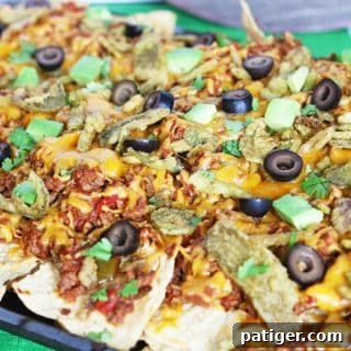 Loaded nachos on a sheet pan topped with cheese, beef, olives, cilantro, and avocado.