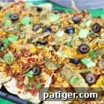 Loaded nachos on a sheet pan topped with cheese, beef, olives, cilantro, and avocado.