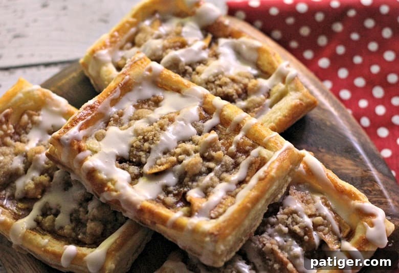 A freshly baked apple danish recipe with a delicious crumb topping and a delicate drizzle of icing, presented beautifully on a platter. This tasty apple crumb danish makes for a sweet breakfast or brunch option.