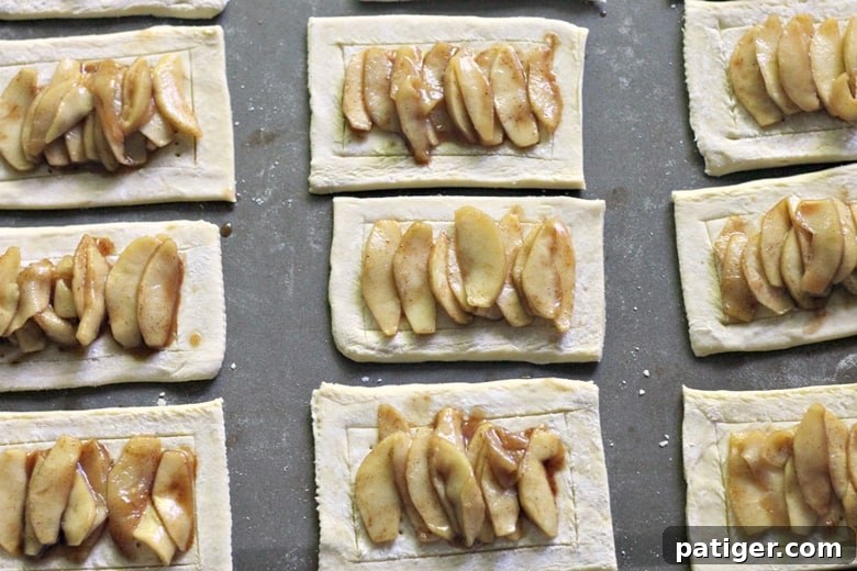 A close-up view of making apple crumb danishes, with apple filling spooned onto puff pastry and ready for crumb topping.