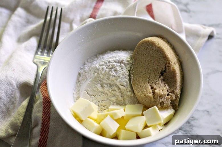 A bowl containing the ingredients for crumb topping: brown sugar, flour, and softened butter, ready to be mixed.