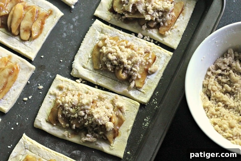 In-process image of making apple danishes with crumb topping sprinkled over the apple filling, ready for baking.