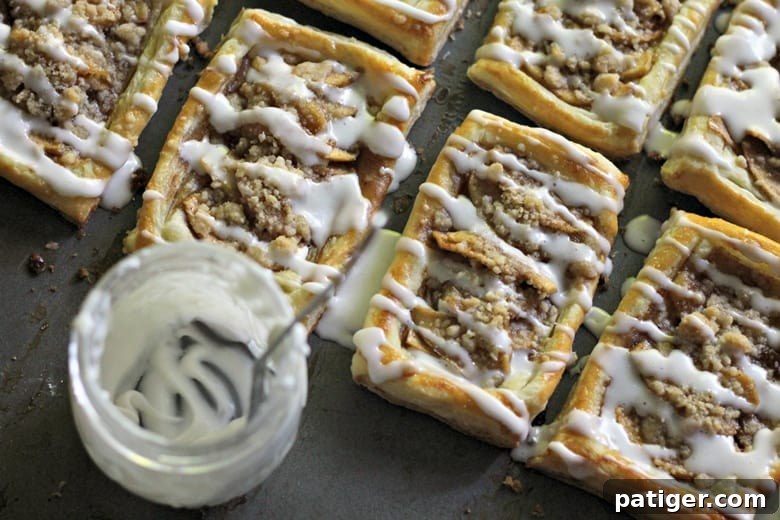 Several apple danishes freshly drizzled with white icing, showcased beautifully on a surface.