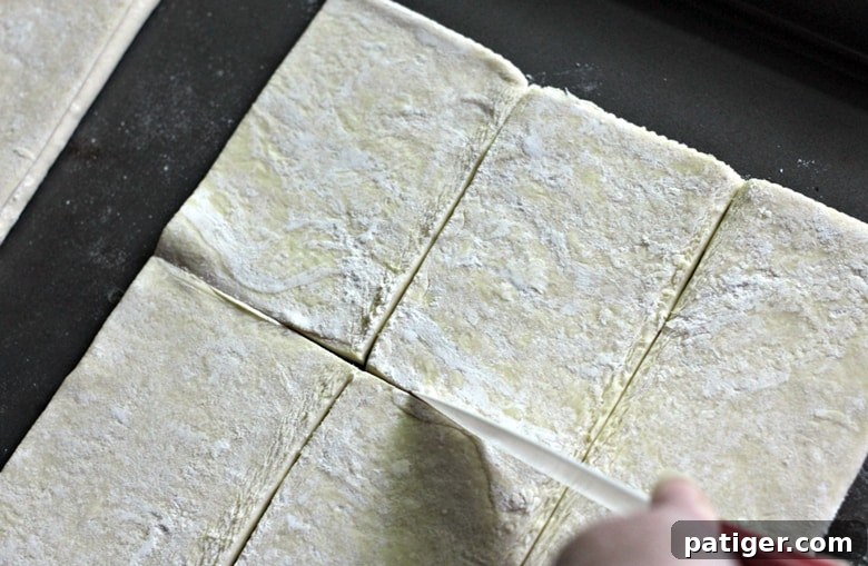 Puff pastry being cut into 12 rectangular pieces on a work surface, a step in making apple danishes.