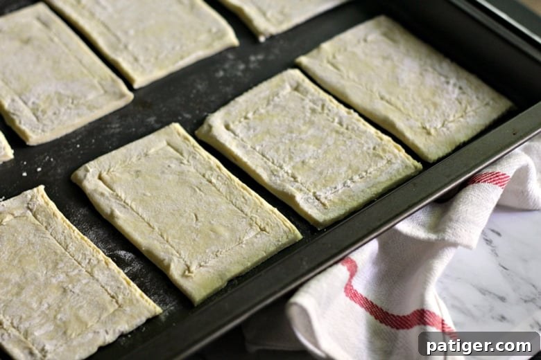 A close-up image showing a knife scoring a border around the edge of each puff pastry rectangle, creating a defined edge for the apple filling.