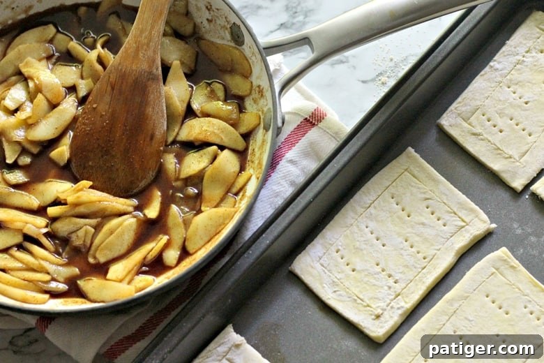 A pan of cooked apple filling sits beside a tray of prepared rectangular pieces of puff pastry, ready for assembly into apple danishes.
