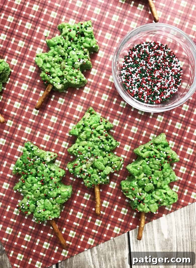 Close-up of a festive green Christmas Tree Rice Krispie Treat with pretzel stick trunk and colorful sprinkles.