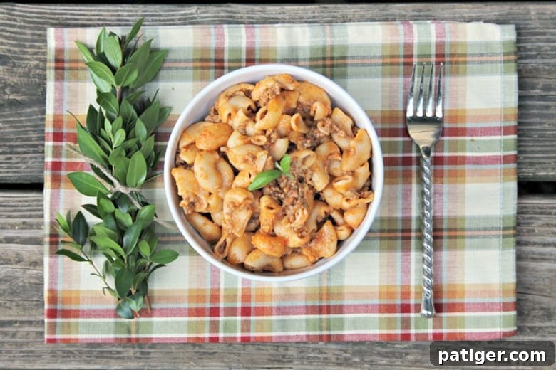 Bowl of Instant Pot Cheesy Hamburger Casserole on a placemat with a fork and fresh herbs for garnish