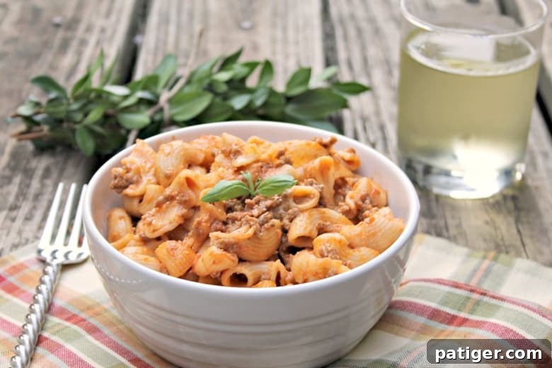 Bowl of Instant Pot Cheesy Hamburger Casserole on a placemat next to a glassed beverage, ready to eat.
