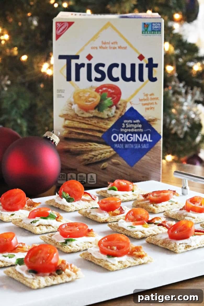 Festive Triscuit Bites 5 Close-up of a single Triscuit cracker topped with cream cheese, a piece of bacon, and a cherry tomato slice, garnished with parsley.
