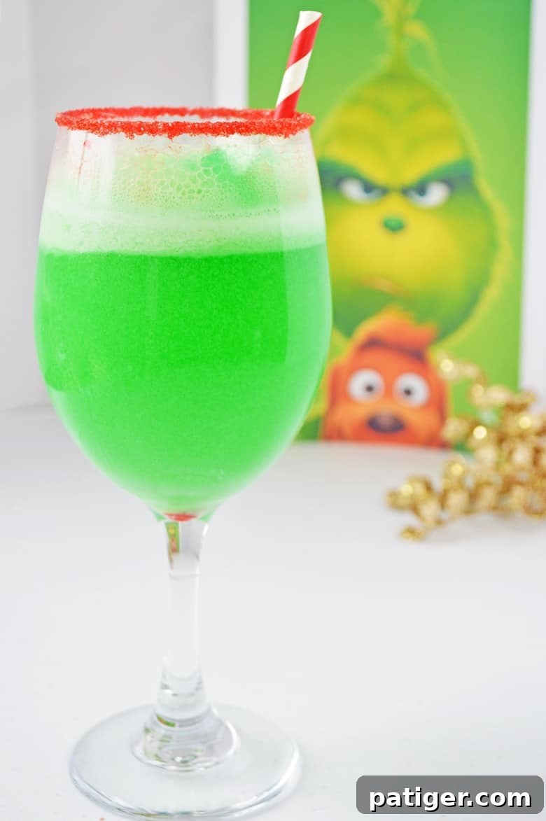 Bright green non-alcoholic Grinch punch in a red sugar-rimmed wine glass with a picture of The Grinch in the background, perfect for Christmas celebrations.