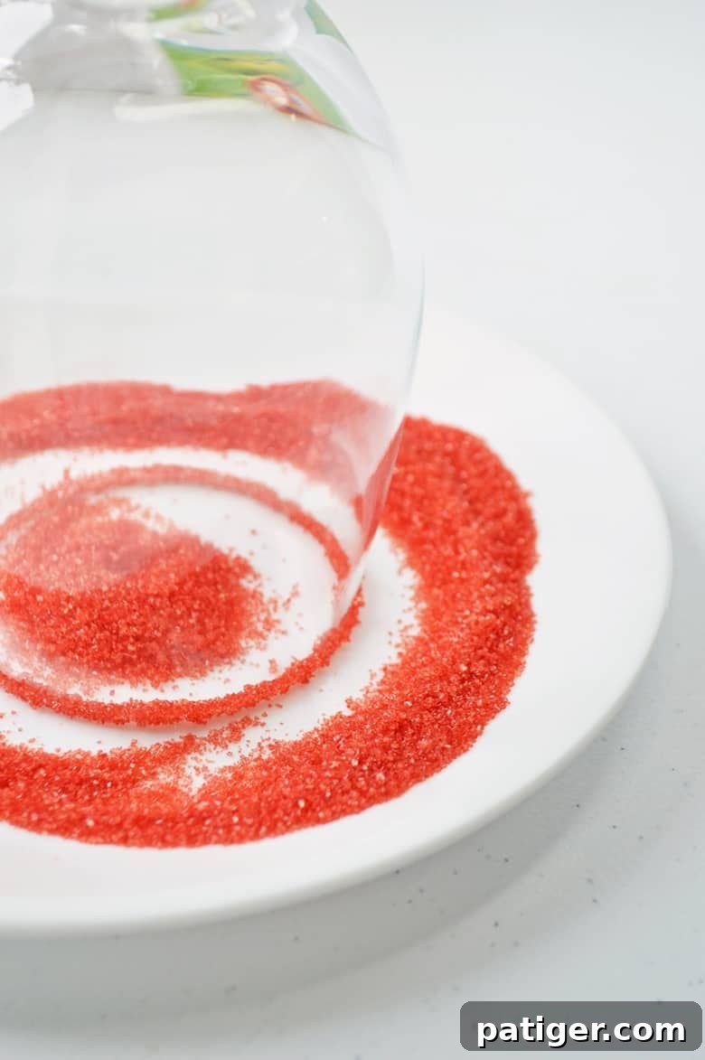 An upside-down wine glass being dipped into a shallow bowl of vibrant red sanding sugar to create a festive rim for the Grinch punch.