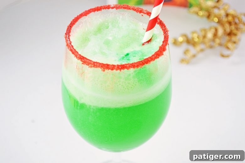 A vibrant green non-alcoholic holiday drink, Grinch punch, served in a wine glass with a festive red sugar rim.