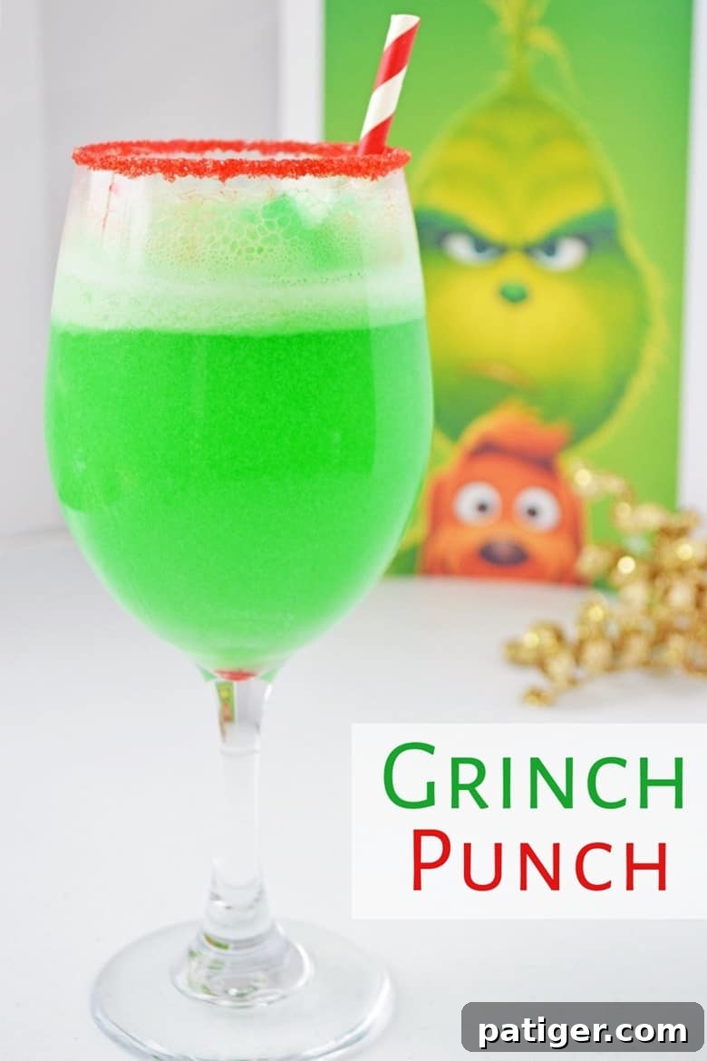A bright green Grinch punch served in a red sugar-rimmed wine glass, with a Grinch character picture in the background, ready for Christmas celebrations.