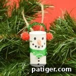 Wine cork decorated to look like a snowman hanging on a christmas tree.