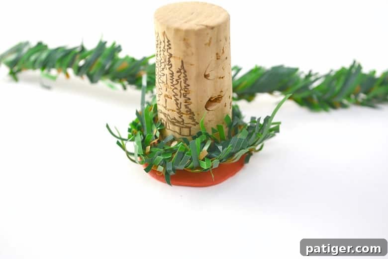 Handmade Wine Cork Candle Ornaments 5 A wine cork delicately wrapped with a length of vibrant artificial pine garland, forming a miniature festive wreath at its base.