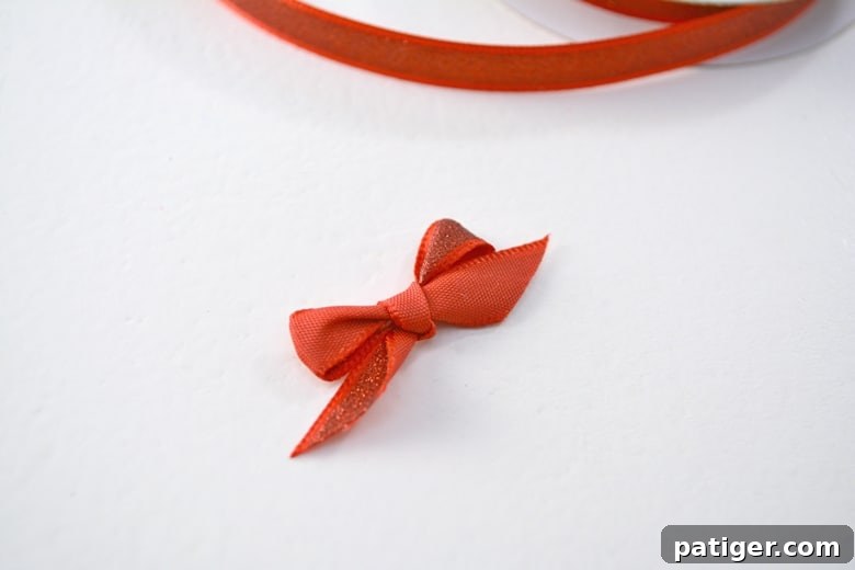 Handmade Wine Cork Candle Ornaments 7 A beautifully tied small red ribbon bow, featuring neat loops and crisp tails, captured against a neutral background.