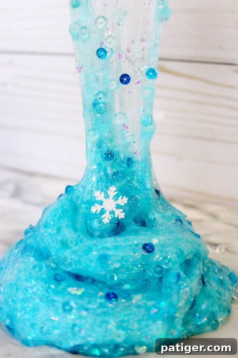 A child's hands playing with sparkly blue Frozen themed slime, featuring glitter and snowflake charms.