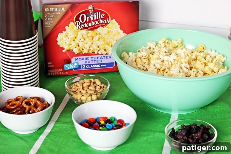 Tailgate Treat: Speedy Sweet and Salty Mix with Custom Football Holders 5 Box of Orville Redenbacher's Popcorn, bowl of popcorn, brown cups, peanuts, chocolate candies, pretzels, and raisins
