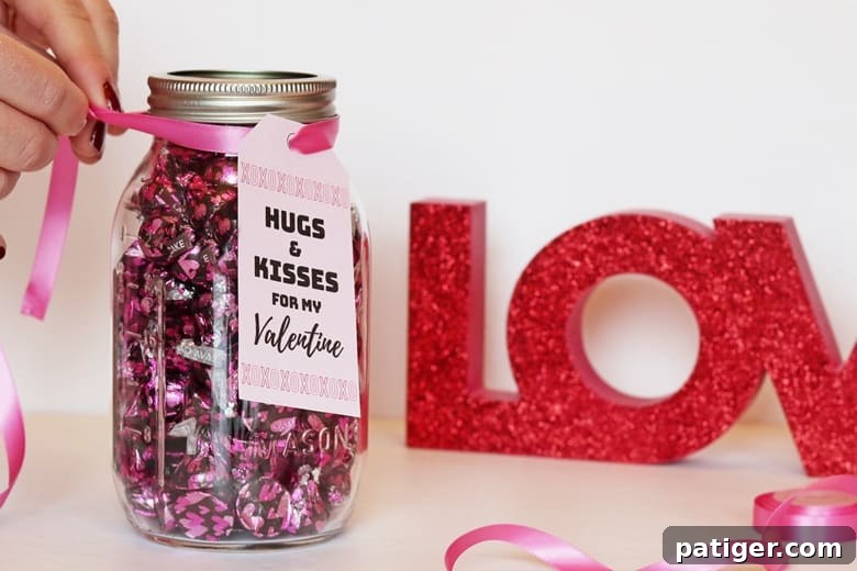 Completed DIY "Hugs & Kisses" mason jar Valentine gift with Hershey Kisses and a tied printable tag.
