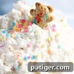 A cheerful teddy graham cookie dipping into a bowl of creamy Funfetti cake batter dip, inviting delight.